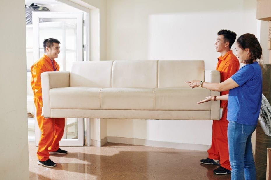 Two movers carrying white sofa being directed by a lady