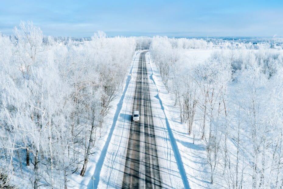 Aerial view of winter road with a car and snow covered trees.